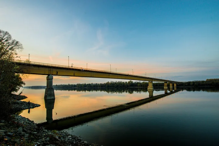 A long bridge reflected in calm water beneath a softly coloured evening sky