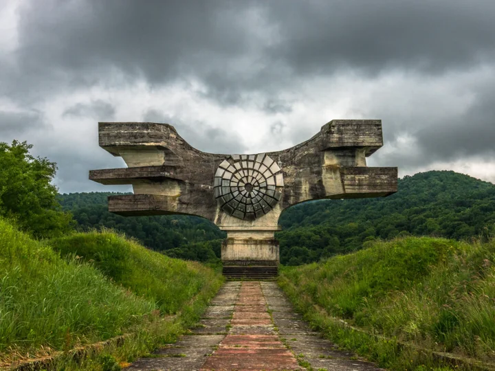 A wing-shaped concrete monument at the end of a paved path beneath dark clouds